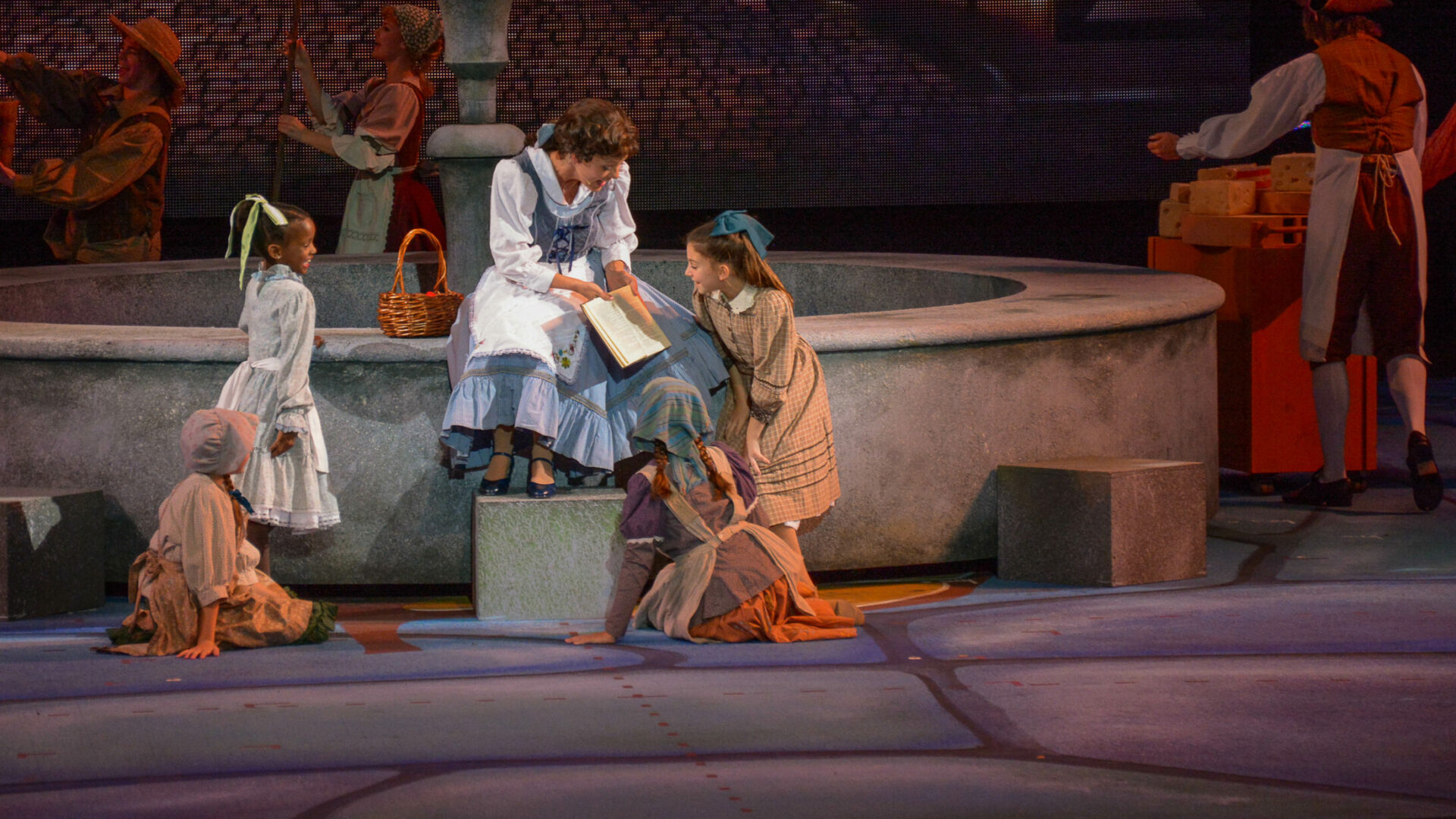 On Stage Photo of Bell from Beauty and The Beast reading to children by a fountain