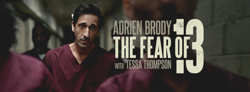 A man in maroon prison scrubs walks down a dimly lit hallway. Large text reads: Adrien Brody The Fear of 13 with Tessa Thompson. The scene appears tense and dramatic.